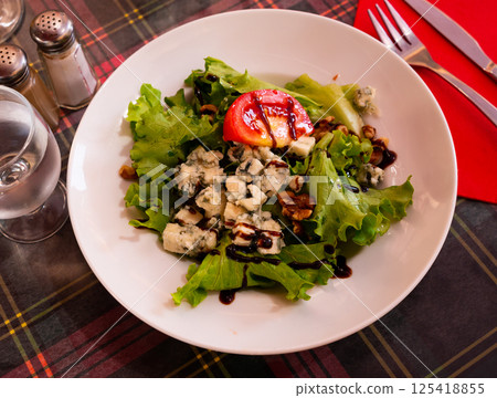Plate with salad with lettuce, nuts, tomato and brie cheese on table 125418855