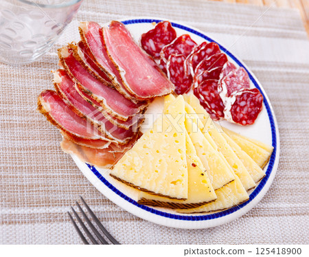 Slices of cheese, sliced smoked sausage and ham on plate. Traditional meat delicacies 125418900