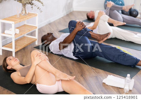 Multinational women and men practicing upward boat pose of yoga on black mat in fitness room 125418901