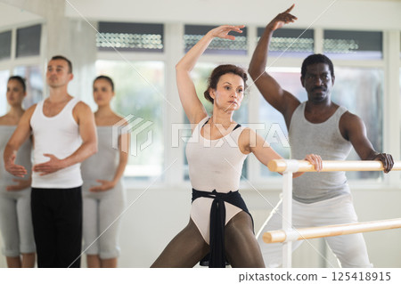 Female ballet instructor practicing demi plie at barre with students 125418915