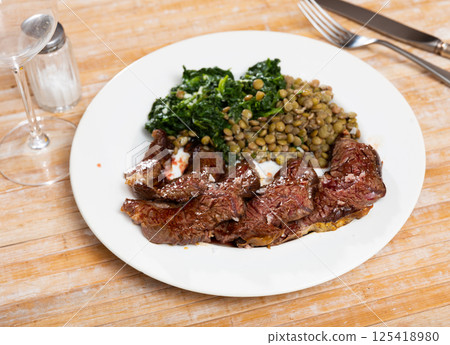 Beef with lentils and spinach served on platter 125418980