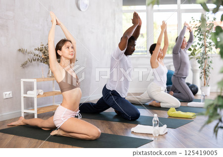 Woman doing Ardha Kapotasana with raised hands during group yoga Woman doing Ardha Kapotasana with raised hands during group yoga 125419005