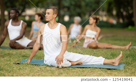 Man performing twisting asana Vakrasana during group yoga in park Man performing twisting asana Vakrasana during group yoga in park 125419041