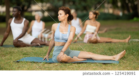 Woman performing Vakrasana during group yoga in summer park Woman performing Vakrasana during group yoga in summer park 125419091