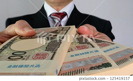 A businessman handing a wad of bills 125419157