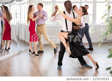 Elegant couple performs an expressive tango in bright, modern dance studio during group class Elegant couple performs an expressive tango in bright, modern dance studio during group class 125419181