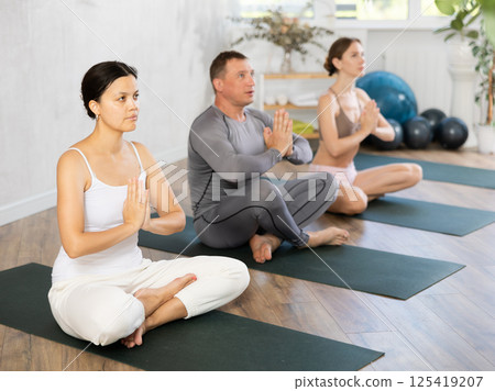 Asian woman sitting in lotus position with hands in namaste during group yoga Asian woman sitting in lotus position with hands in namaste during group yoga 125419207