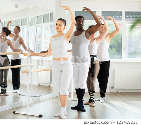 Group ballet rehearsal - men and women stand in third position near ballet barre during group training in dance studio 125419213