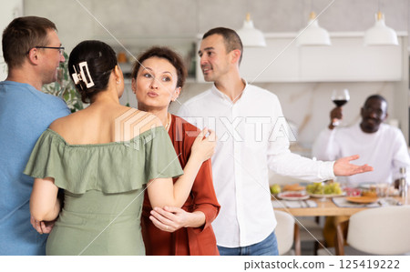 Smiling woman giving greeting kiss to bestie at dinner party 125419222