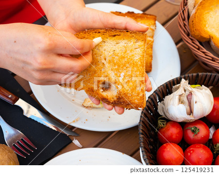 Female hands rubbing toast with garlic while preparing Pan Con Tomate 125419231