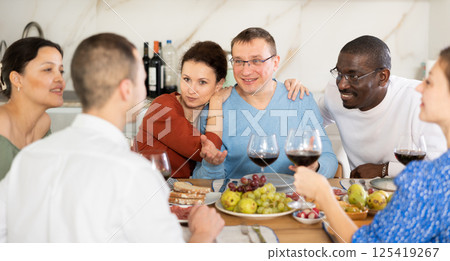 Companions congregated around a festive table, participating in animated discussions and enjoying the delights of red wine 125419267