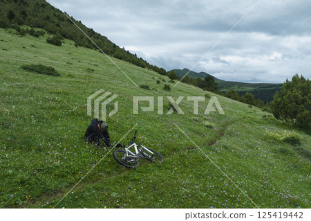 Aerial view of woman riding mountain bike on flowering grassland mountain trail Aerial view of woman riding mountain bike on flowering grassland mountain trail 125419442
