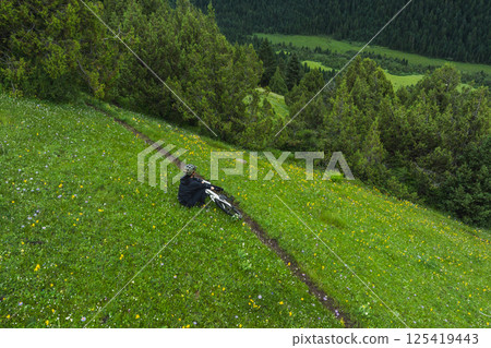 Aerial view of woman riding mountain bike on flowering grassland mountain trail 125419443