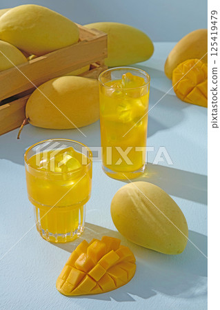 Mango juice is served in different shaped glasses, presented on a blue background. Ripe mangoes are scattered around and filled in a wooden crate. mango cross section is cut into even squares. Mango juice is served in different shaped glasses, presented on a blue background. Ripe mangoes are scattered around and filled in a wooden crate. mango cross section is cut into even squares. 125419479