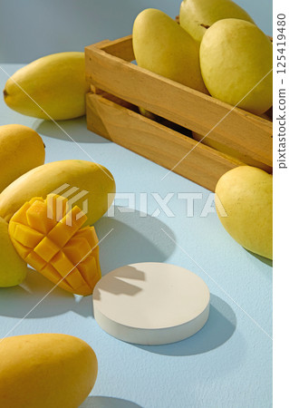Empty round podium is placed in the middle to display the products. Ripe mangoes are placed around and filled in a brown wooden crate. The Alphonso mango fruit flesh is sliced into even dices. 125419480