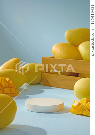 Empty podium with mangoes placed around. Mangoes are a tropical fruit rich in vitamins, diced into fresh, ripe pieces. Blue background with light shining on it, shows the shadows of mangoes. 125419481