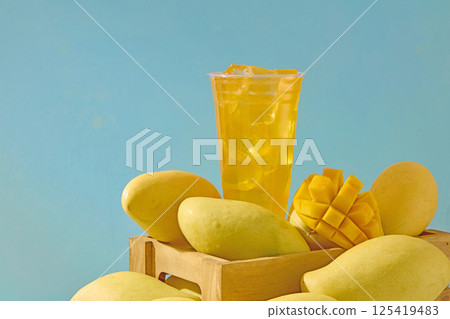 Ripe mangoes with greenish yellow skin, placed in wooden crates, freshly harvested from the farm. Mangoes are stacked on top of each other, diced mangoes placed around a glass of mango juice. Ripe mangoes with greenish yellow skin, placed in wooden crates, freshly harvested from the farm. Mangoes are stacked on top of each other, diced mangoes placed around a glass of mango juice. 125419483