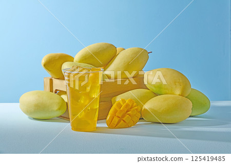 Ripe mangoes with greenish yellow skin, placed in wooden crates, freshly harvested from the farm. Mangoes are stacked on top of each other, diced mangoes placed around a glass of mango juice. Ripe mangoes with greenish yellow skin, placed in wooden crates, freshly harvested from the farm. Mangoes are stacked on top of each other, diced mangoes placed around a glass of mango juice. 125419485
