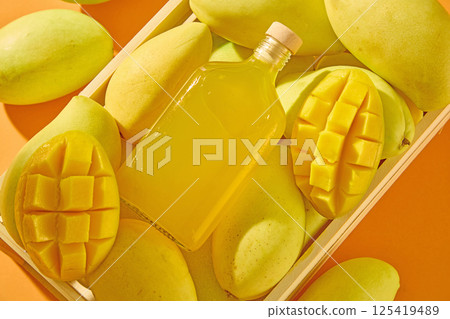 Top view of a glass bottle containing mango juice, without a label for advertising. Bottle is placed on the mango background. The mango is cut in half to reveal a juicy flesh, scored into squares. 125419489