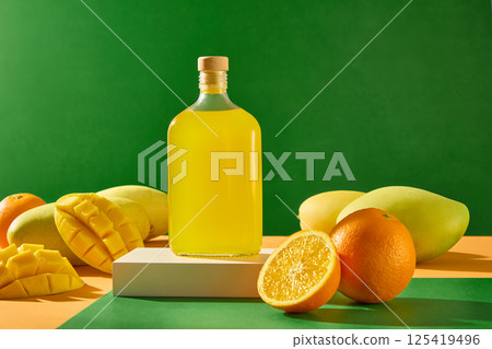 A juice bottle stands on a stone pedestal, its label blank for design purposes. Mango slices lie on ripe mangoes. The orange in the foreground has been cut in half to reveal its juicy segments. 125419496