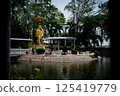 Singburi, Thailand, March 23, 2025, Golden statue of serene figure beside a reflective pond in Wat Phikun Thong, amidst lush greenery 125419779