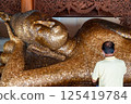 Singburi, Thailand, March 23, 2025, Visitors admire the serene golden reclining Buddha at Wat Phra Non Chak Si Worawihan 125419784