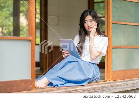 一位年輕女子手裡拿著平板電腦思考 125420668