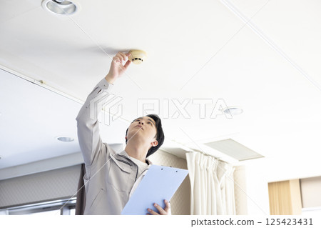 建築維護:一名身穿工作服的男子正在檢查火災警報裝置 建築維護:一名身穿工作服的男子正在檢查火災警報裝置 125423431