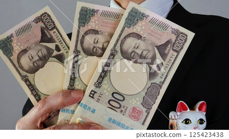 A businessman holding a stack of bills and a maneki-neko (beckoning cat) 125423438