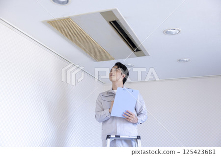 Building maintenance: A man in work clothes inspecting an air conditioner 125423681