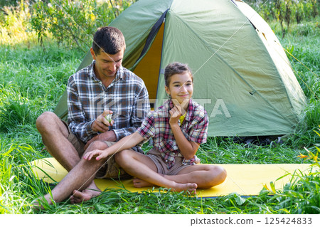 Dad sprays repellent on daughter outdoor camping and picnicking near a tent Dad sprays repellent on daughter outdoor camping and picnicking near a tent 125424833