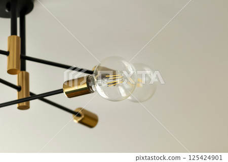 Stylish chandelier with exposed filament light bulbs, set against a bright white background, showcasing modern lighting equipment and interior design aesthetics in daylight Stylish chandelier with exposed filament light bulbs, set against a bright white background, showcasing modern lighting equipment and interior design aesthetics in daylight 125424901