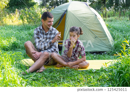 Dad sprays repellent on daughter outdoor camping and picnicking near a tent Dad sprays repellent on daughter outdoor camping and picnicking near a tent 125425011