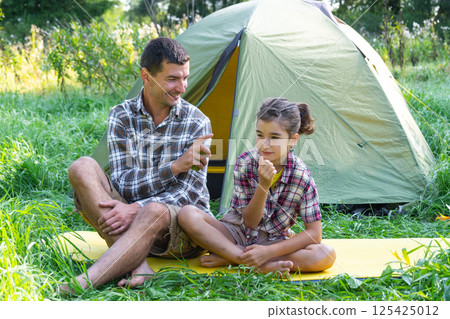 Dad sprays repellent on daughter outdoor camping and picnicking near a tent Dad sprays repellent on daughter outdoor camping and picnicking near a tent 125425012