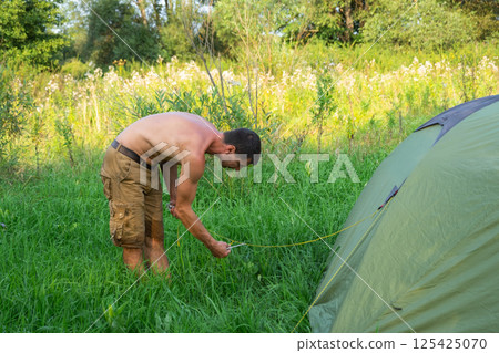 The man installs and assembles tourist tent in a camping in nature in the forest. Domestic tourism, active summer holidays, family adventures. Ecotourism, sport, hike The man installs and assembles tourist tent in a camping in nature in the forest. Domestic tourism, active summer holidays, family adventures. Ecotourism, sport, hike 125425070
