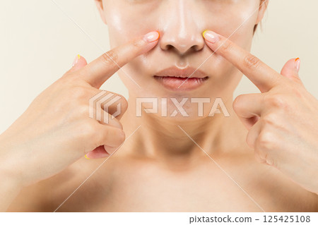 Close-up of the face of a young Asian woman pointing at her nose. 125425108