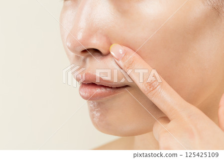 Close-up of the face of a young Asian woman pointing at her nose. 125425109