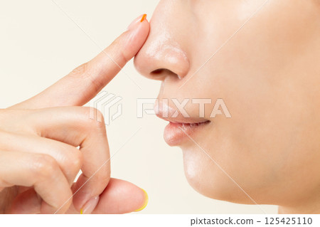 Close-up of the face of a young Asian woman pointing at her nose. Close-up of the face of a young Asian woman pointing at her nose. 125425110