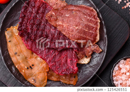 Jerky, dried meat in the form of slices with salt, spices and herbs Jerky, dried meat in the form of slices with salt, spices and herbs 125426551