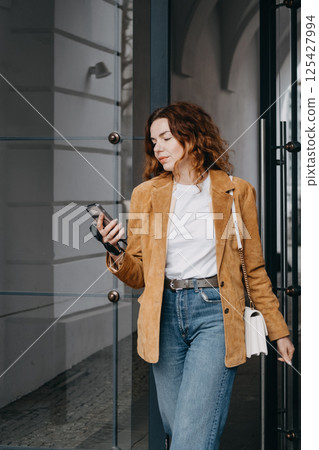 Tech-savvy woman engaging in mobile-first lifestyle outside modern building. Smartphone habits, mobile productivity, and digital behavior.. 125427994