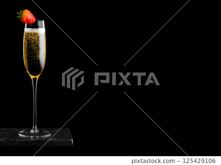 Elegant glass of yellow champagne with strawberry on top on black marble board on black background. 125429106