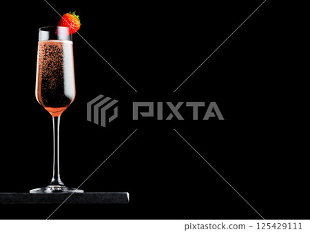 Elegant glass of pink rose champagne with strawberry on top on black marble board on black 125429111