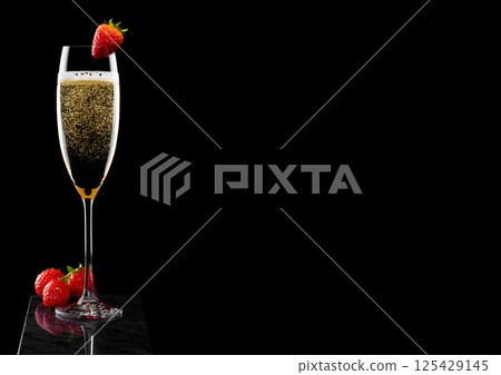 Elegant glass of yellow champagne with strawberry on top and fresh berries on black marble board Elegant glass of yellow champagne with strawberry on top and fresh berries on black marble board 125429145