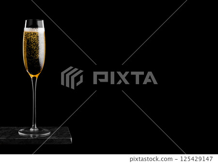 Elegant glass of yellow champagne with bubbles on black marble board on black background. Elegant glass of yellow champagne with bubbles on black marble board on black background. 125429147