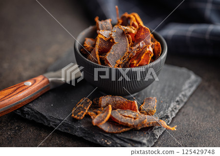 Beef jerky. Dried spiced meat on black table. 125429748