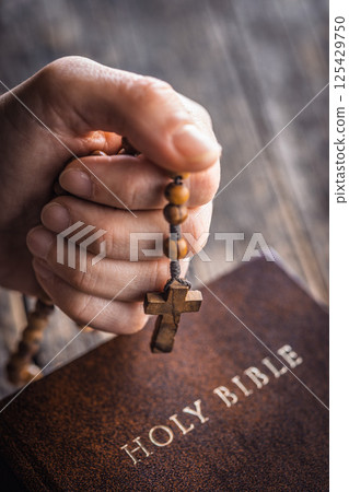 Hand holding a rosary in front of the Holy Bible. 125429750