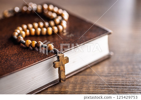 Wooden rosary beads and Holy Bible on wooden table. 125429753
