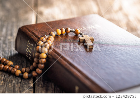 Wooden rosary beads and Holy Bible on wooden table. 125429755