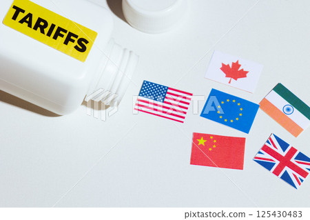 Tariff-labeled pill bottle spilling global trade flags Tariff-labeled pill bottle spilling global trade flags 125430483