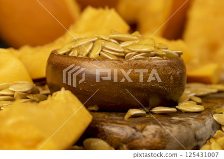 seeds of ripe orange pumpkin, large pumpkin seeds that have just been removed from a cut pumpkin, seeds in a wooden bowl, side view 125431007